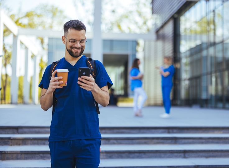 Male healthcare professional smiling at his phone drinking coffee