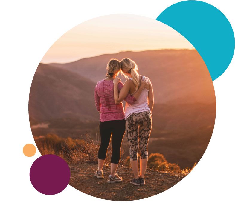 Two woman hugging while staring at sunset